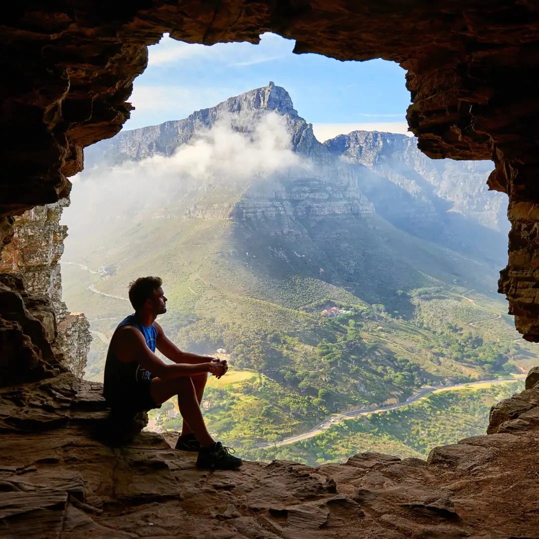 Traveller sitting in a cave opening overlooking mountains